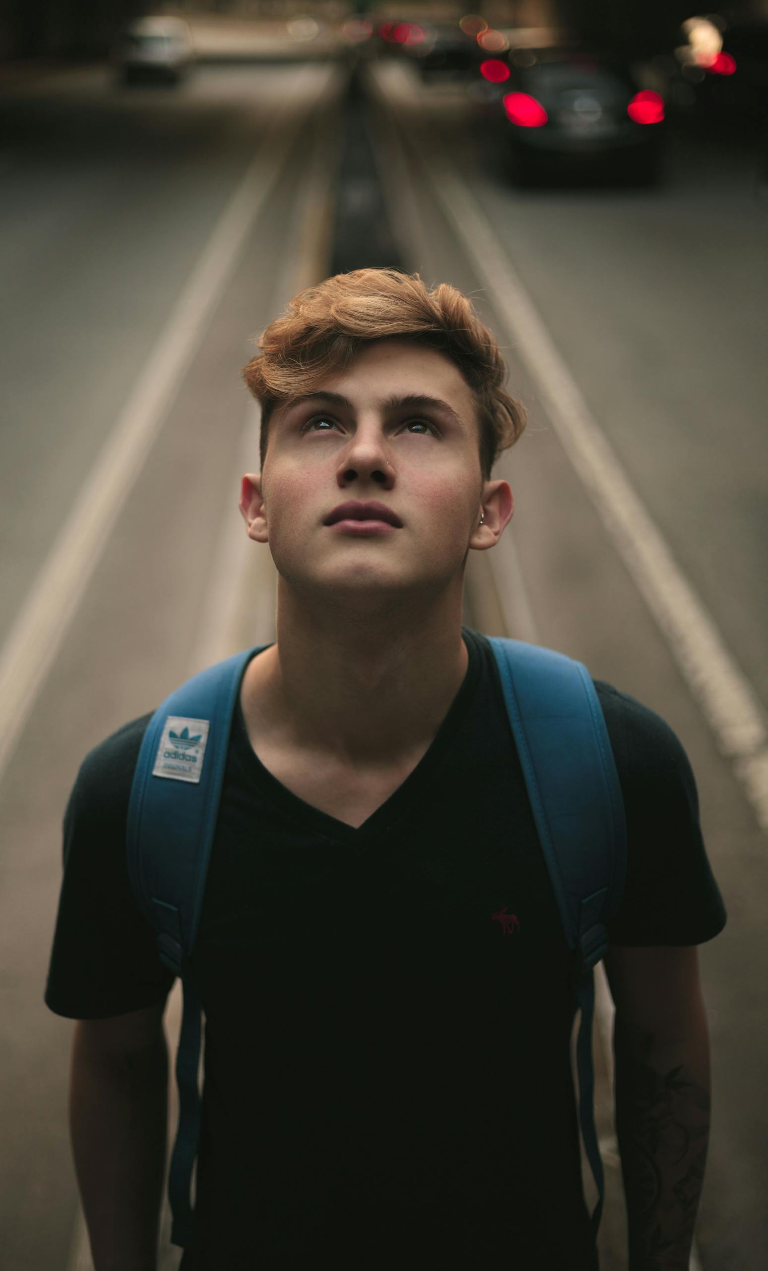 Portrait of a young man looking up in a city street with blurred traffic background.